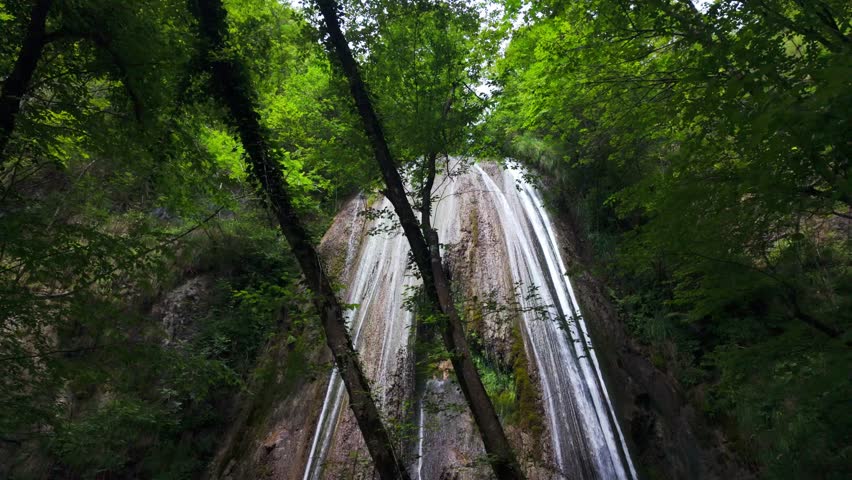 Tall Forest Waterfall Cascading Down Rocky Cliff in Natural Wilderness