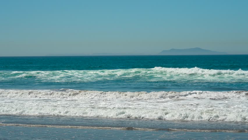 Blue ocean waves roll on Channelside beach with an island on the horizon