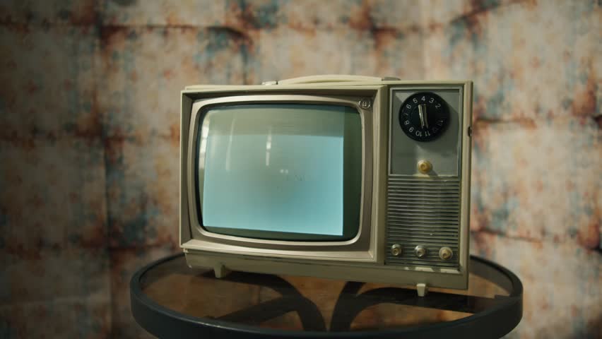 A vintage television flickers with nostalgic black and white static, surrounded by warm lighting and classic decor. This setup evokes memories of past technologies and cozy evenings
