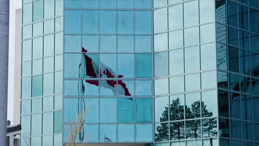 A Canadian flag waves on a building in downtown Halifax. It reflects on the glass as people pass by. This shows pride and connection to Canada in Nova Scotia