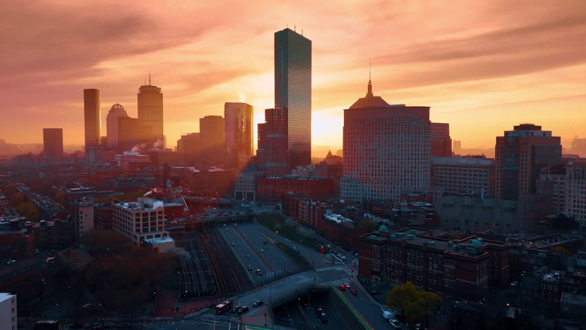 Bright setting sun shines from behind the skyscrapers. Drone footage over the downtown of Boston, Massachusetts, USA at sunset.