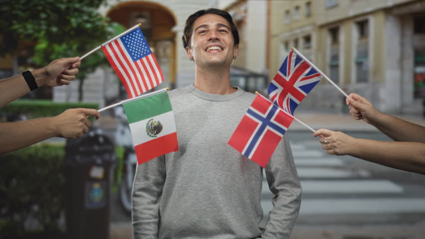 Man smiles with eyes closed as multiple national flags are waved around him on a street; solidarity joy.