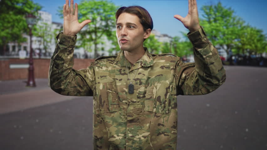 Man in camouflage with dogtag and hands raised on a street, puckering lips while showing open palms; pride duty loyalty.
