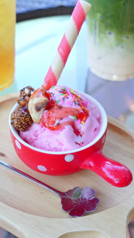Pink strawberry ice cream scoop in a red polka dot bowl topped with syrup and sprinkles.