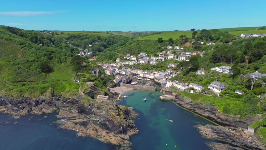 Aerial wide shot capturing the scenic historic fishing village of Polperro with its small sheltered harbour water inlet surrounded by densely wooded hillsides and white buildings in Cornwall, United Kingdom. Polperro, United Kingdom