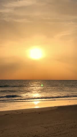 Experience a breathtaking golden sunset gracefully descending over the calm ocean, casting a warm, ethereal glow across the gentle waves and sandy beach. This tranquil scene reflects nature