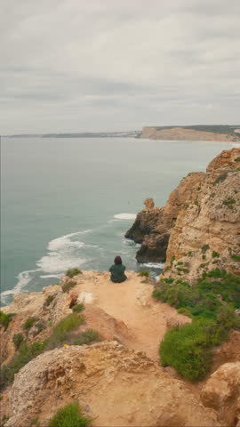 A woman sits on a high cliff on Portugal