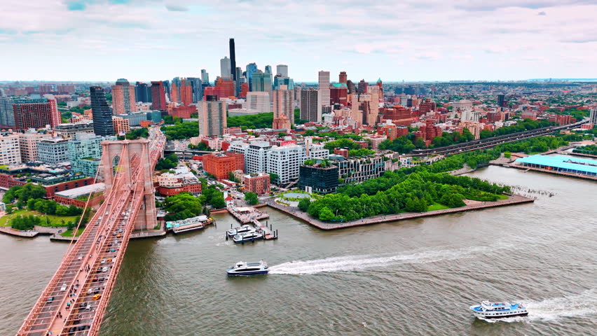 Motor boat heading towards the Brooklyn Bridge with busy traffic on. Beautiful waterfront of New York, USA from aerial perspective.