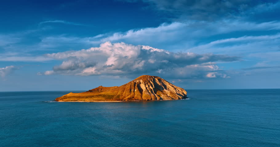 Little rocky island under the beautiful fluffy cloudscape. Approaching the Rabbit Island near Oahu, Hawaii, USA.