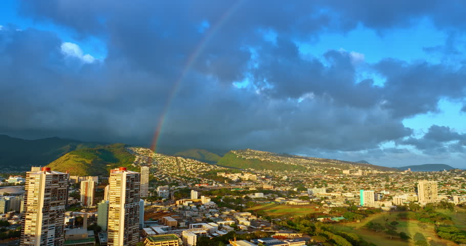 Fantastic view of rainbow over the green mountains at the backdrop of rainy cloudscape. Rising over the scenery of Honolulu, Hawaii, USA at sunset.