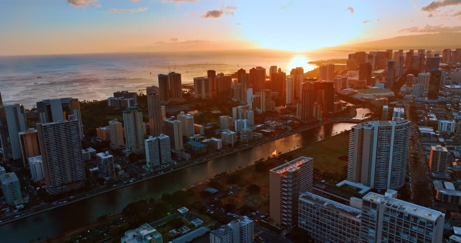 Sun sets over the horizon in the Pacific Ocean. Drone footage above the cityscape of Honolulu, Hawaii, USA at sunset.