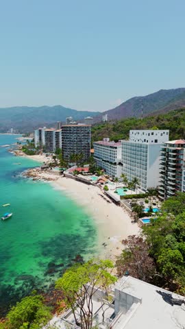 Aerial view of Las Gemelas Beach with luxury hotel resorts along the turquoise coastline and lush green hills in Puerto Vallarta, Jalisco, Mexico.