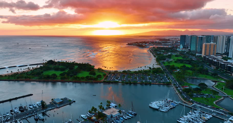 Spectacular view of setting sun over the Pacific Ocean. Picturesque shore of Honolulu, Hawaii, USA with beautiful park area. Aerial perspective.