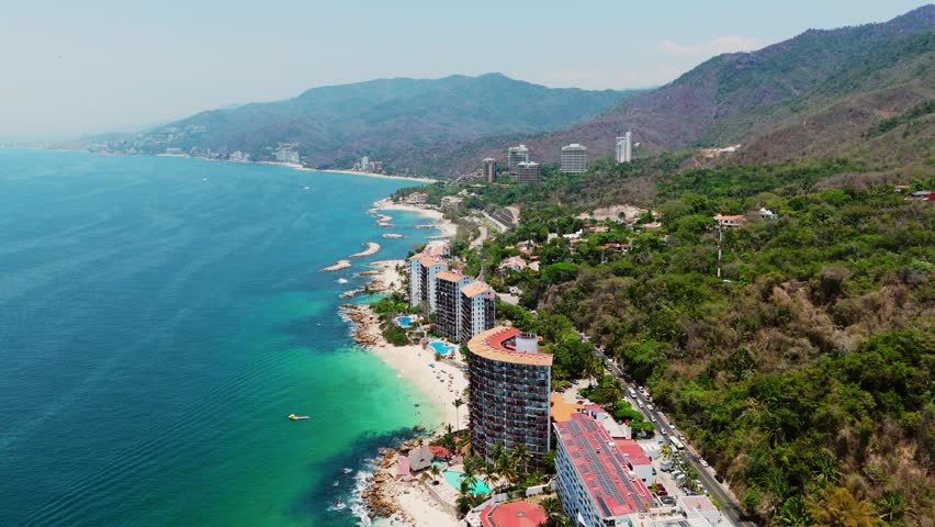 Aerial view of Las Gemelas Beach with high-rise resorts, turquoise ocean water, and lush green mountains in Puerto Vallarta, Jalisco, Mexico.