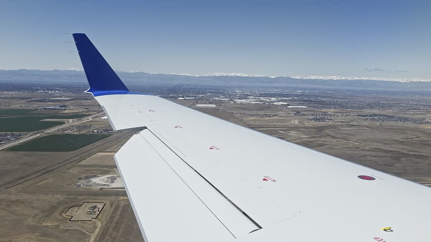 Airplane Wing Over Denver Landscape And Snowy Rocky Mountains, Travel video frame showing aircraft descent above plains, city and distant peaks