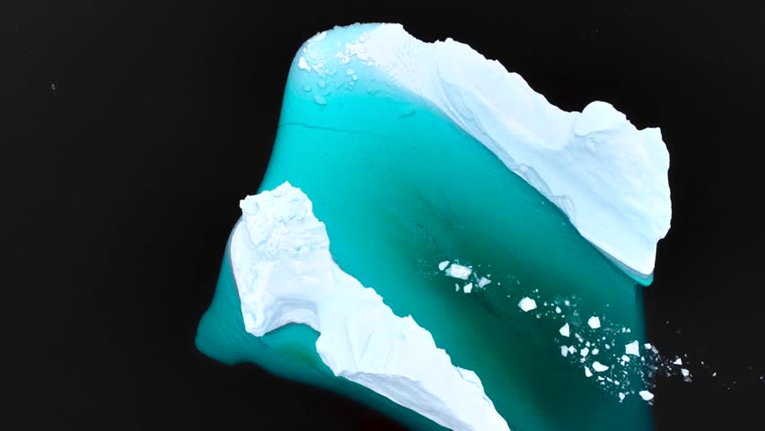 Aerial view of a massive iceberg with vibrant turquoise submerged ice floating in the dark arctic waters near Tasiilaq, Sermersooq Municipality, Greenland.