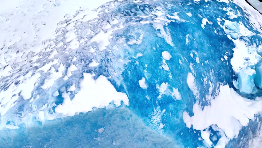 Aerial view of the textured surface of a massive iceberg with deep blue glacial ice and white snow in Tasiilaq, Sermersooq Municipality, Greenland.