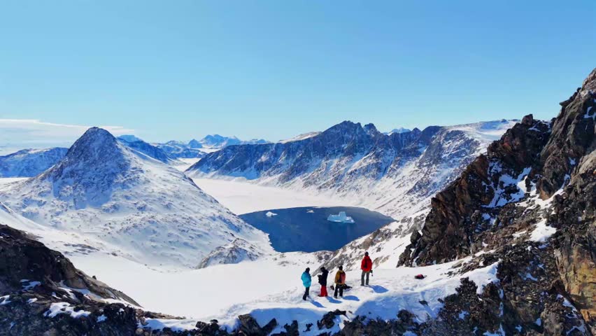 Aerial view of a group of people standing on a snowy mountain ridge overlooking a fjord with icebergs in Tasiilaq, Sermersooq Municipality, Greenland.