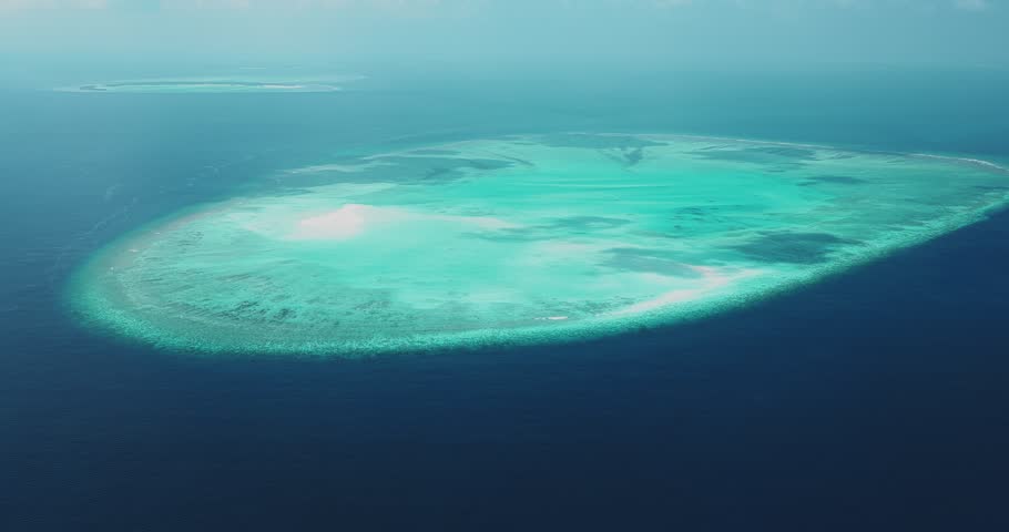 Aerial view of a vibrant coral reef atoll with turquoise lagoon waters surrounded by the deep blue Indian Ocean near Dhidhdhoo, Haa Alif, Maldives.