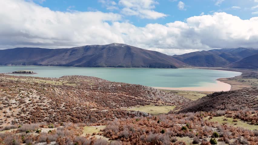 Wide angle aerial tracking shot moving forward over rugged autumn hills, revealing the turquoise bay of Lake Prespa, Maligrad Island, and rolling Balkan mountain ranges