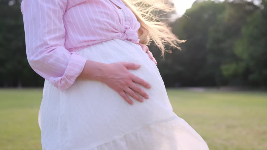 Pregnant woman touching her belly at sunset