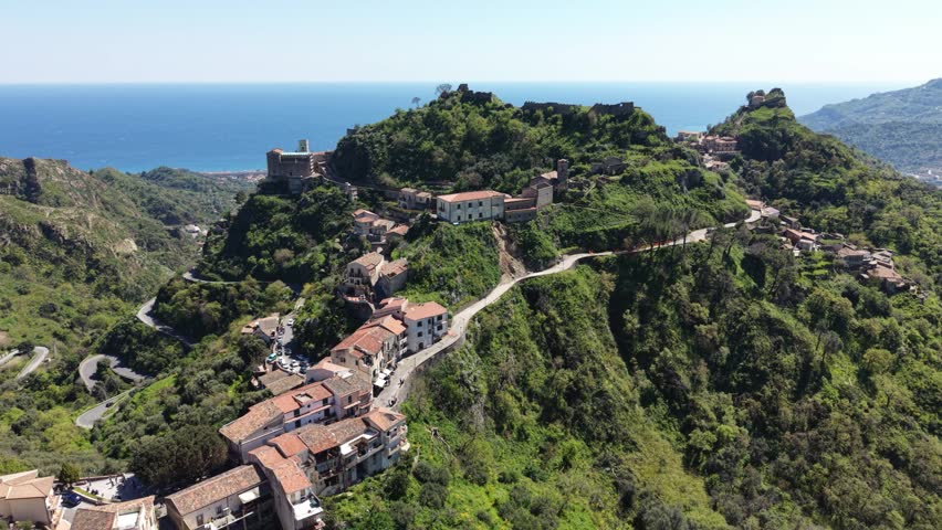 Aerial view of the historic hilltop village of Savoca with stone houses and winding roads overlooking the Mediterranean Sea in Savoca, Sicily, Italy.