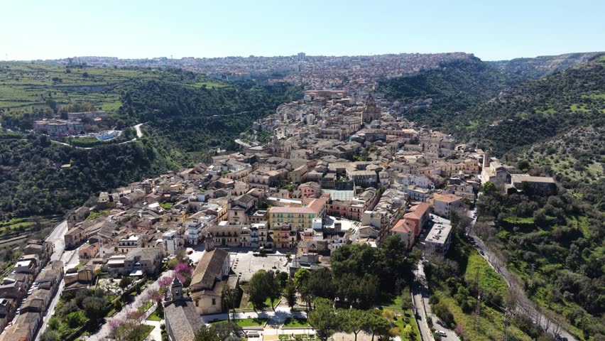 Aerial view of the historic stone buildings and rooftops of Ragusa Ibla nestled in the green valleys of Sicily, Ragusa, Sicily, Italy.
