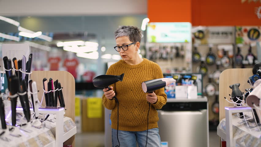 Mature woman choosing hair dryer in appliance store with discount