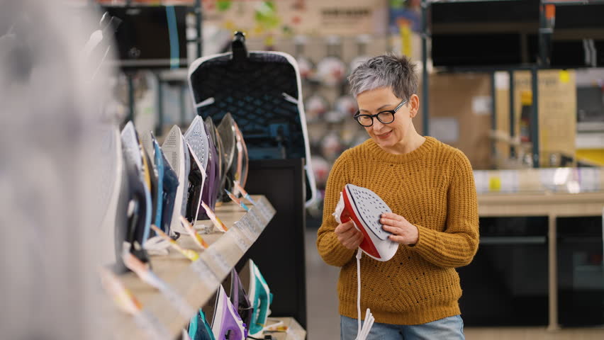 Mature woman choosing new iron in appliance store on Black Friday