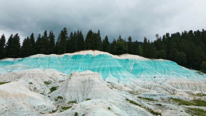 Unusual turquoise blue clay hills in a forest landscape under a cloudy sky