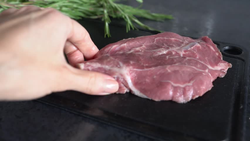 A woman’s hand places fresh steaks on a chopping board. Close-up.