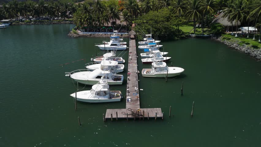 Yachts and sailboats dock near Puerto Quetzal cruise pier in Guatemala. Calm water reflects masts beside a rustic restaurant cottage shaded by trees. Pacific breeze moves through, blending marina life with coastal dining views.