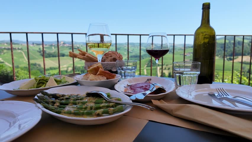 A table set with wine and appetizers overlooks rolling green hills in the Italian countryside.