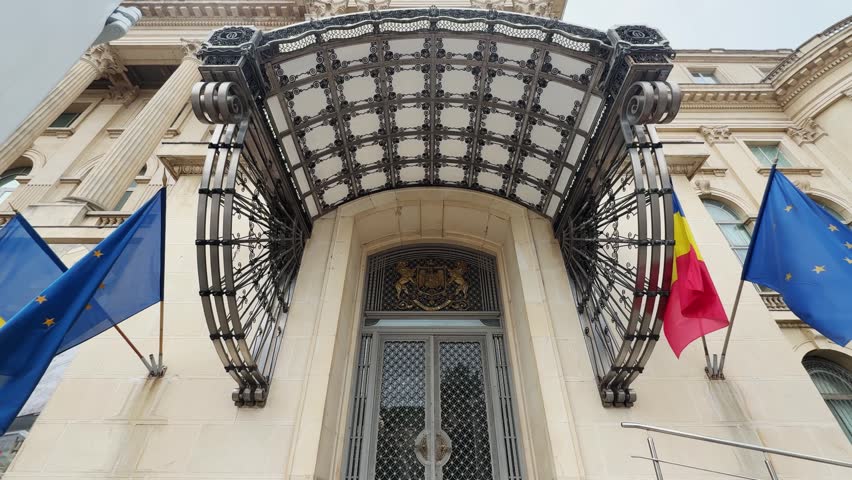 Grand entrance of the Royal Palace, now National Museum of Art, in Bucharest, Romania. Features intricate ironwork canopy and multiple national flags.