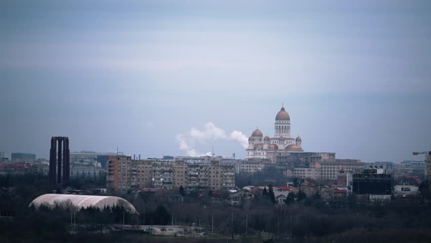 An authentic aerial view captures the majestic Catedrala MÃ¢ntuirii Neamului dominating the evolving cityscape of Bucharest, Romania, under a cloudy sky. Showcasing urban development and spiritual landmark.