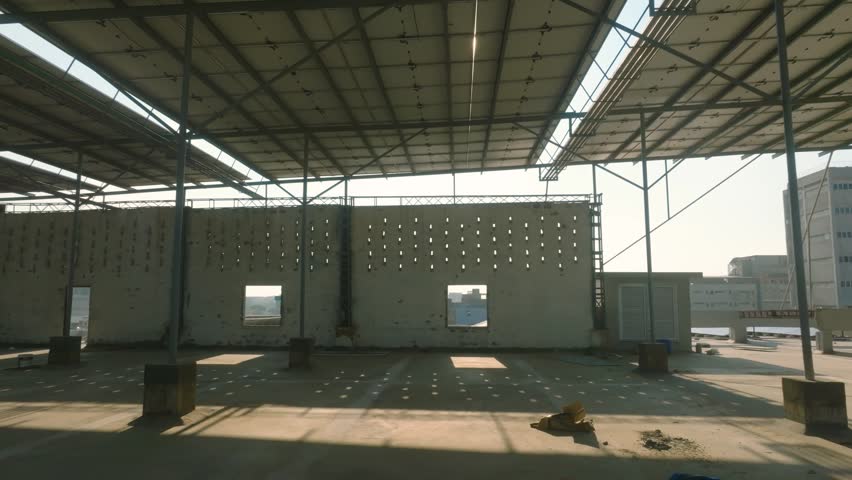 Drone pans beneath a solar canopy as sunlight pierces through, Karachi factory.
