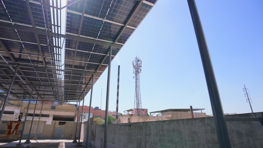 Drone pans beneath an open solar canopy as sunlight streams through, Karachi.