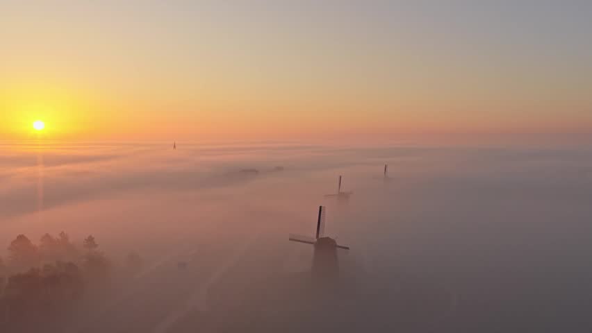 Stunning aerial view of traditional dutch windmills rising above a sea of thick fog during a beautiful and colourful sunrise in holland
