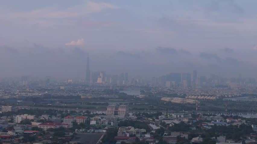 Aerial drone view of a modern city skyline emerging through dramatic morning clouds and mist. Atmospheric urban landscape with skyscrapers and expansive city development.