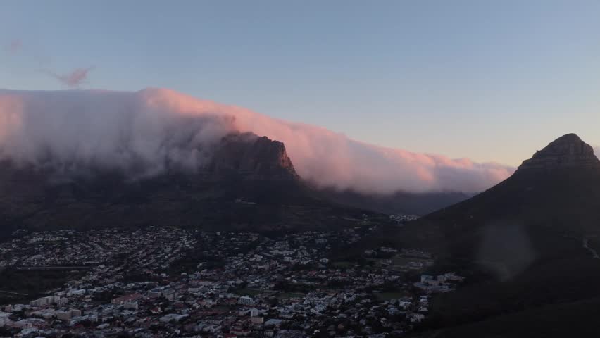 Aerial drone footage of low clouds rolling over Table Mountain with Lion’s Head emerging into frame above Cape Town, South Africa.