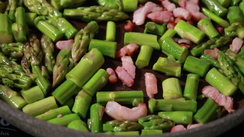 Close-up of fresh green asparagus spears and savory bacon slices sizzling together in a hot frying pan