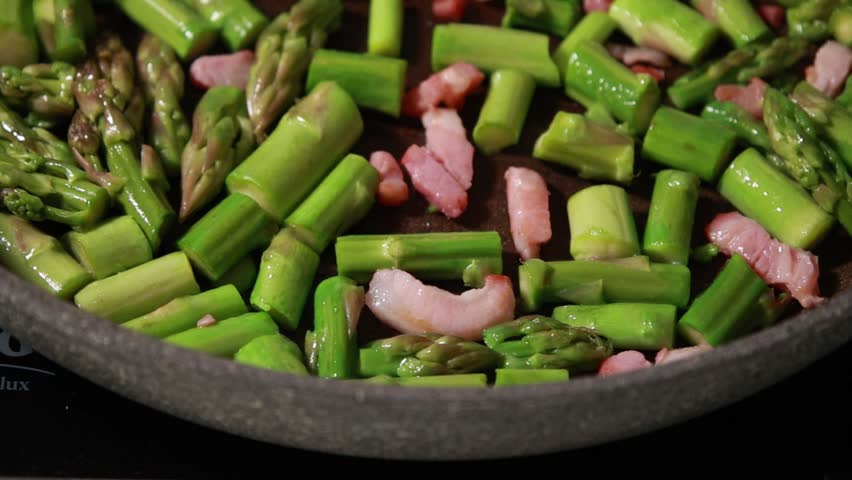 Close-up of fresh green asparagus spears and savory bacon slices sizzling together in a hot frying pan