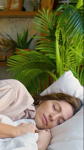 A beautiful Caucasian woman in her forties peacefully sleeping in her pajamas. She gently adjusts her blanket, creating a cozy sanctuary for restful dreams. 30 FPS FHD footage.