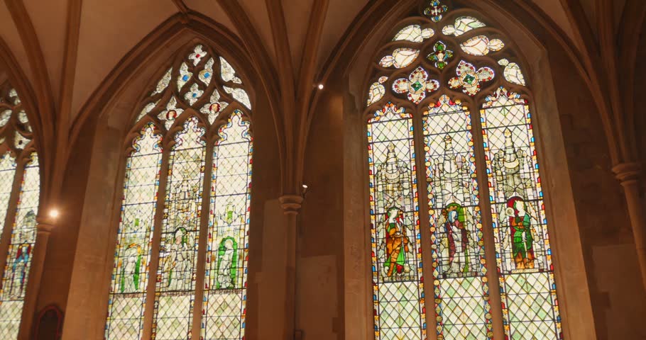 Low-angle shot of ornate medieval stained glass windows inside Christ Church Cathedral, Oxford. Gothic arches and warm stone.