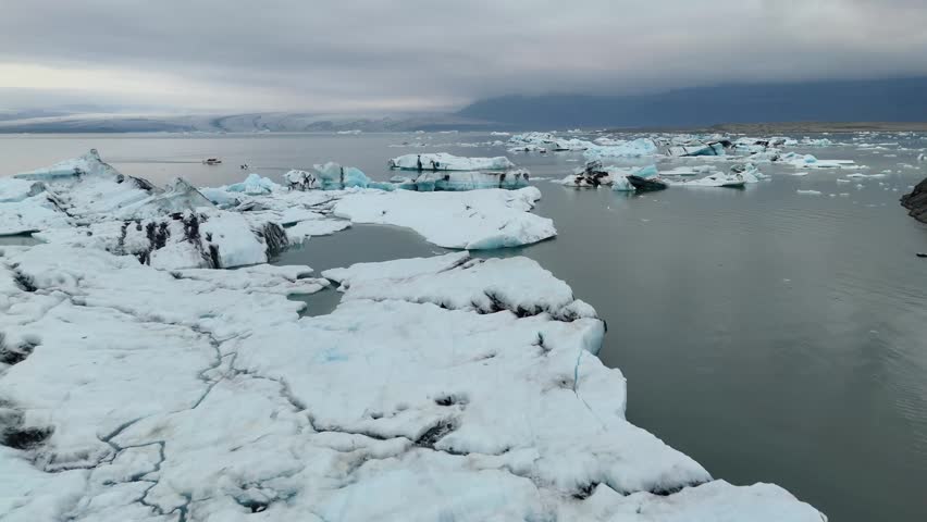 Aerial view of icebergs slowly drifting over the calm blue water of Jokulsarlon Glacier Lagoon in Iceland, creating a cold and peaceful scene.
