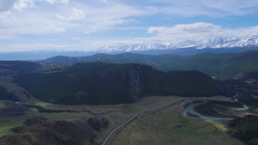 Winding Road Through Green Valley Toward Snowy Peaks