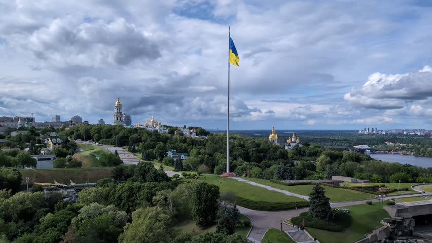 Panoramic scenic view of the giant national flag of Ukraine waving over Kyiv hills and Pechersk Lavra, symbolizing independence and statehood