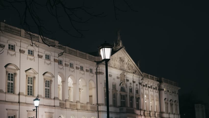 Night view of a magnificent illuminated historical palace in Warsaw, Poland. Ornate architecture and street lamps define the elegant atmosphere after dark.