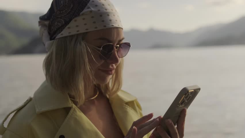 Young woman using a smartphone while traveling across Lake Como, Italy. Scenic lakeside landscape, mountain views and modern travel lifestyle concept.