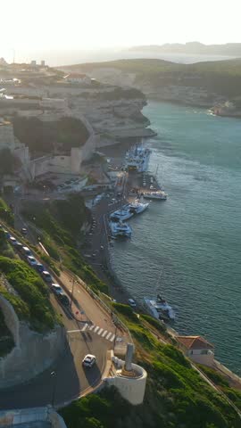 A narrow road on a rocky hill above a harbor with yachts in an ancient maritime town aerial view
